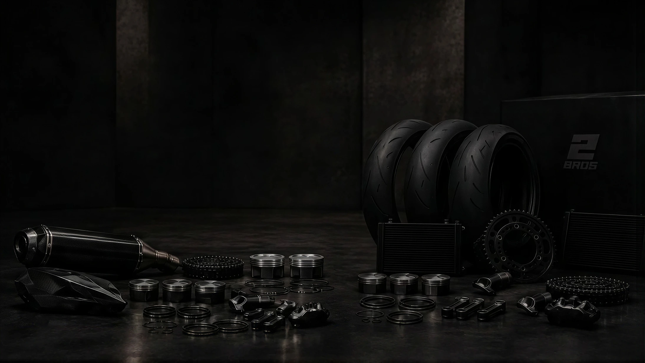 2Bros exhaust, pistons, tyres, sprockets and radiators laid out in a dark workshop