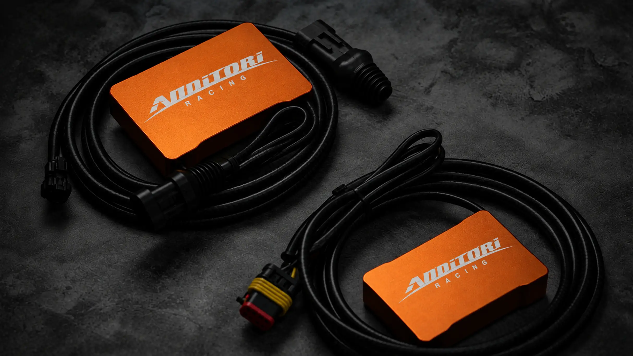 Orange and green Annitori Racing quickshifter units with their wiring looms on dark slate